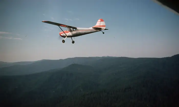 Light aircraft flying over wooded hills